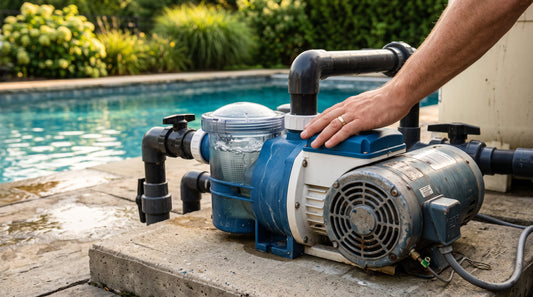 A pool owner rests a hand on a residential pool pump and motor beside an in-ground pool, checking it for noise.